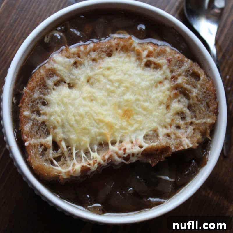 A bowl of rich Crockpot French Onion Soup, topped with a golden, cheesy crouton, next to a spoon.