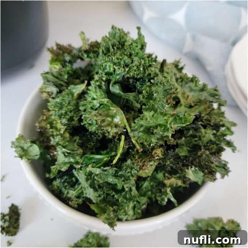 Crispy Air Fryer Kale Chips presented in a white bowl, beside a textured cloth napkin.