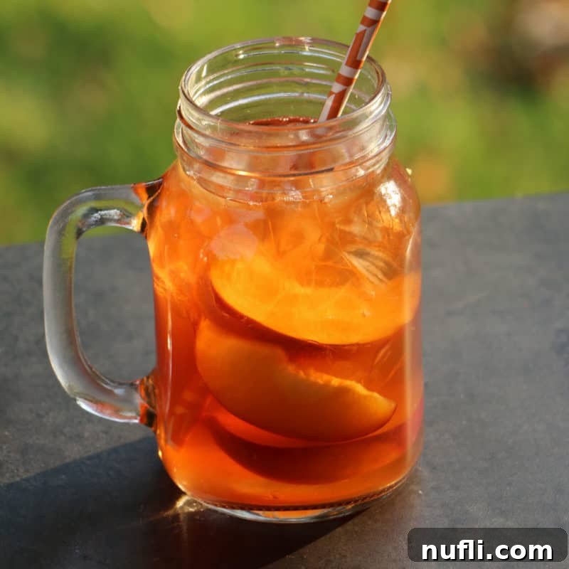 Peach Iced Tea Cocktail in a mason jar glass with sliced peaches and a paper straw