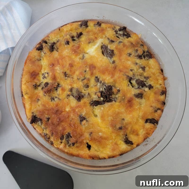 A golden-brown Bisquick Impossible Cheeseburger Pie presented in a clear glass pie pan, with a serving spatula resting nearby, inviting a taste.