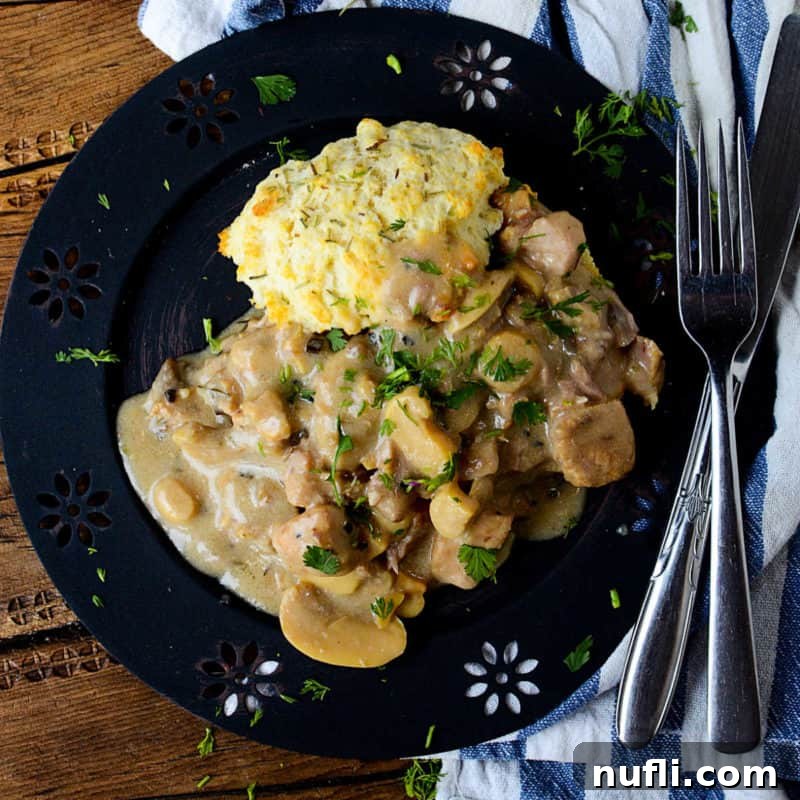A blue plate showcasing a succulent Rosemary Pork Chop with a creamy sauce, served alongside a fork and knife, for a gourmet comfort meal.