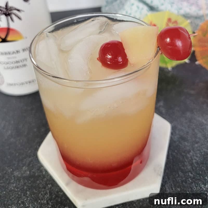 Tropical Pineapple Cocktails Made Easy 11 Malibu sunset drink in a clear glass garnished with maraschino cherries and pineapple chunk