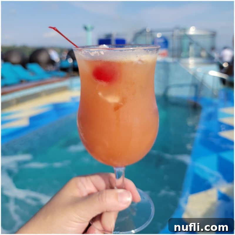 Tropical Pineapple Cocktails Made Easy 17 pink orange cocktail in a hurricane glass with a cherry in front of a pool