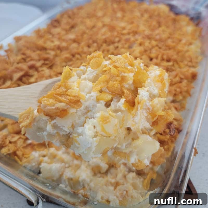 A serving spoon gracefully scooping a portion of Funeral Potatoes from a warm casserole dish, showcasing its cheesy, comforting layers.