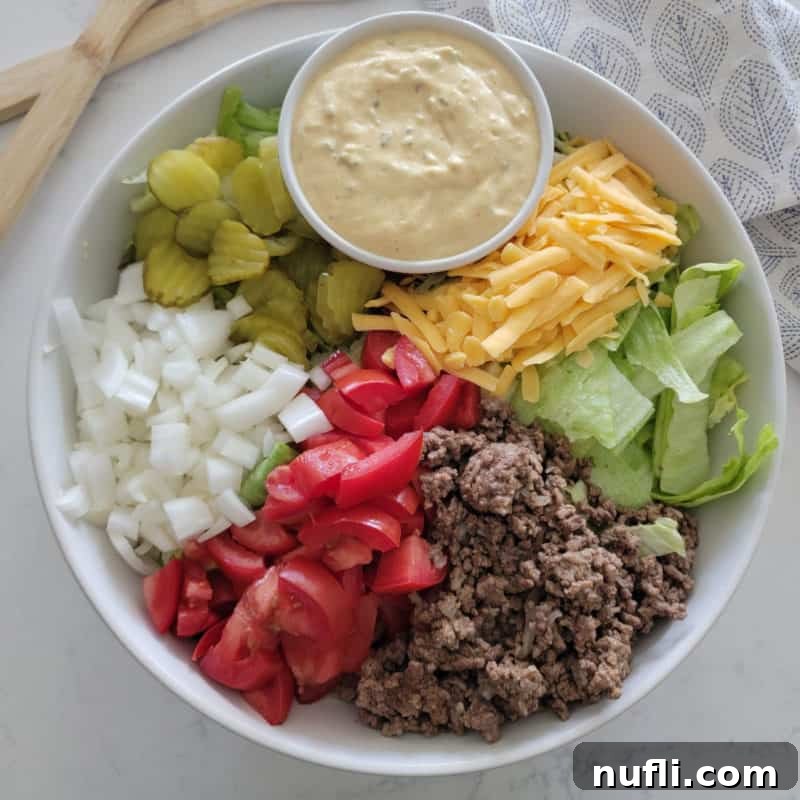 A hearty Big Mac Salad in a white bowl, loaded with ground beef, shredded lettuce, pickles, onions, tomatoes, shredded cheese, and a drizzle of special Big Mac sauce.