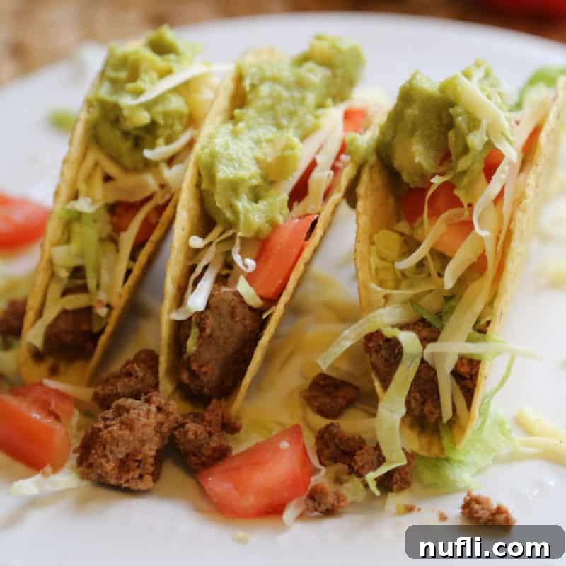 A crispy taco shell filled with savory taco meat, generously topped with shredded lettuce, diced tomatoes, and creamy guacamole.
