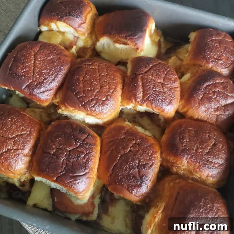 A metal baking pan filled with golden-brown Funeral Sandwich sliders, indicating they are ready for serving.