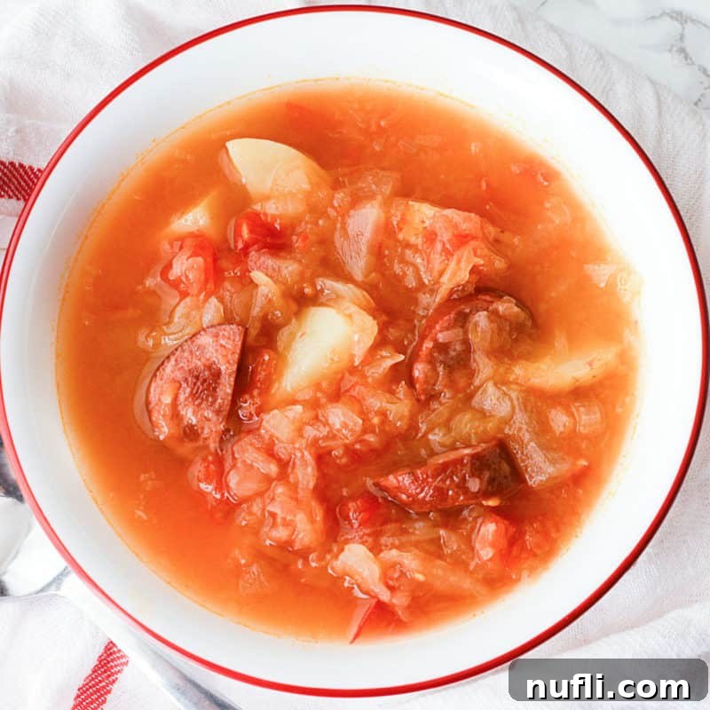A white bowl of hearty Sausage Sauerkraut Soup resting on a cloth napkin, ready to warm you up.