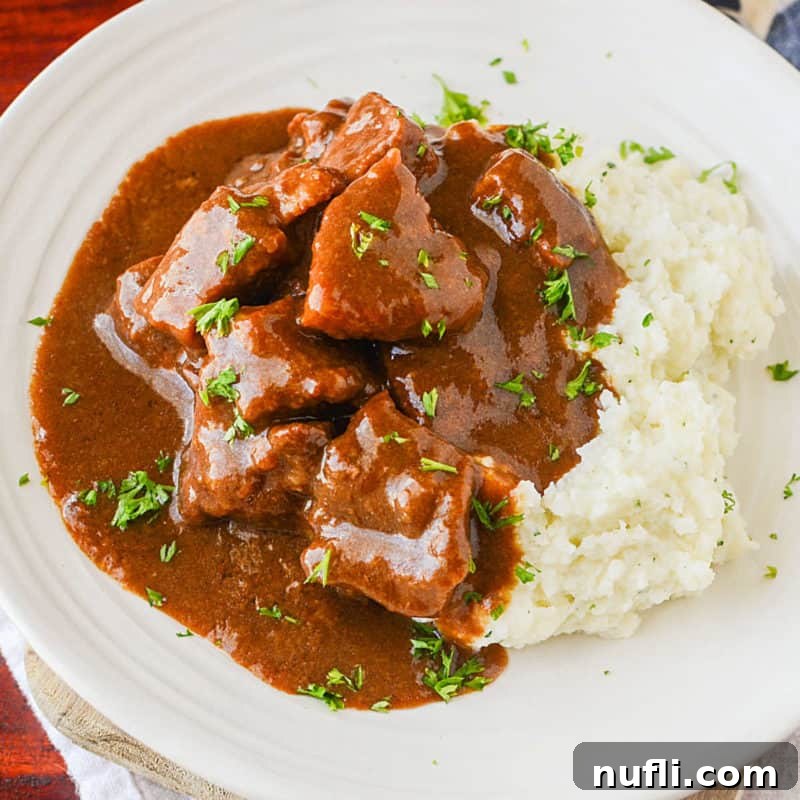 Crockpot Beef Tips and gravy next to potatoes on a white plate