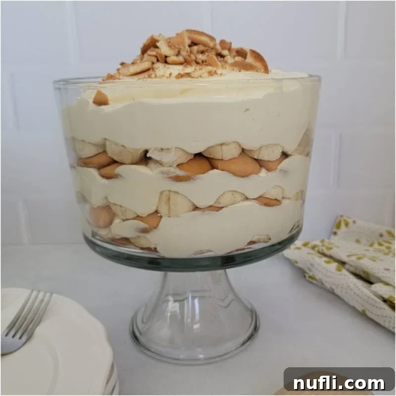 Magnolia Bakery Banana Pudding, artfully layered in a large trifle dish, positioned next to a stack of plates and a cloth napkin.