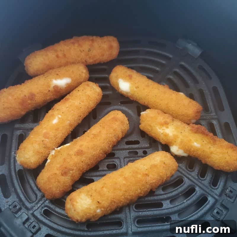 Golden-brown air-fried mozzarella sticks perfectly cooked to crispy perfection within an air fryer basket, ready to be enjoyed.