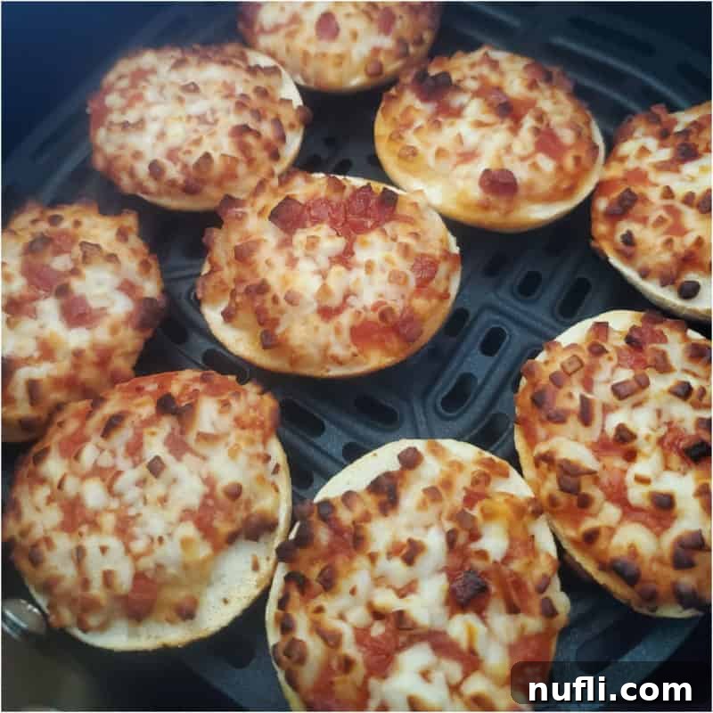 Mini pizza bagel bites evenly spread and cooking to golden perfection in an air fryer basket, promising a crispy texture.