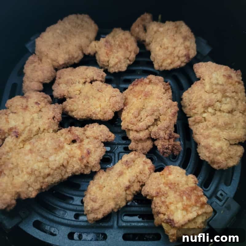 Golden air-fried chicken nuggets, perfectly crispy and evenly spread out in an air fryer basket, ready to be enjoyed as a quick snack.