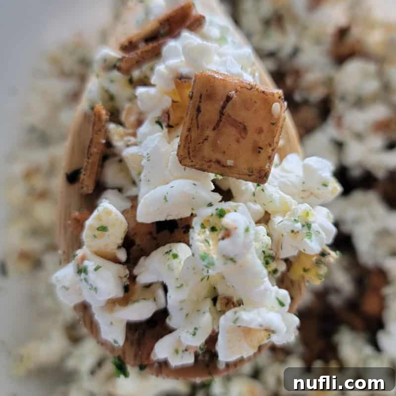 Hawaiian Hurricane Popcorn, a unique and savory snack, being scooped from a large bowl with a wooden spoon, showcasing its intriguing texture and seasonings.