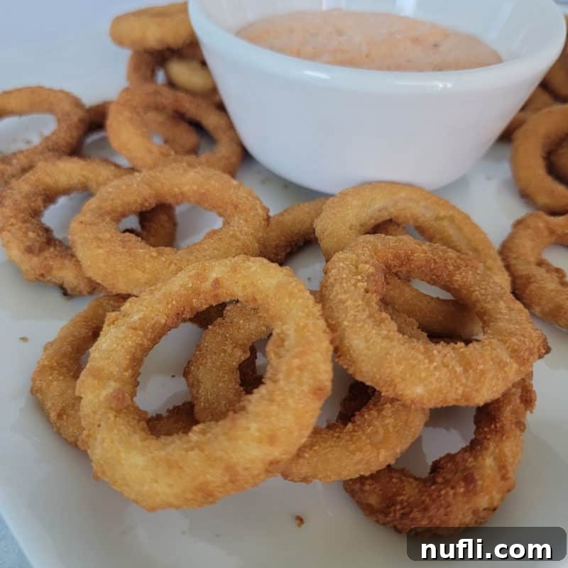 A plate featuring perfectly air-fried onion rings, golden and crispy, accompanied by a small bowl of delicious dipping sauce.