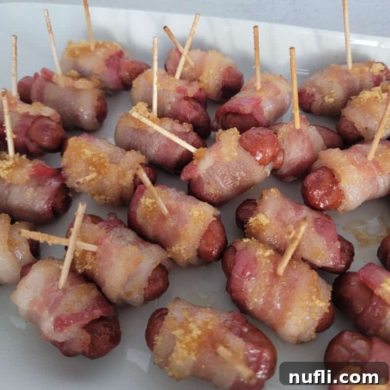 Brown sugar coated bacon-wrapped little smokies, held by toothpicks for easy serving, arranged enticingly on a pristine white platter.