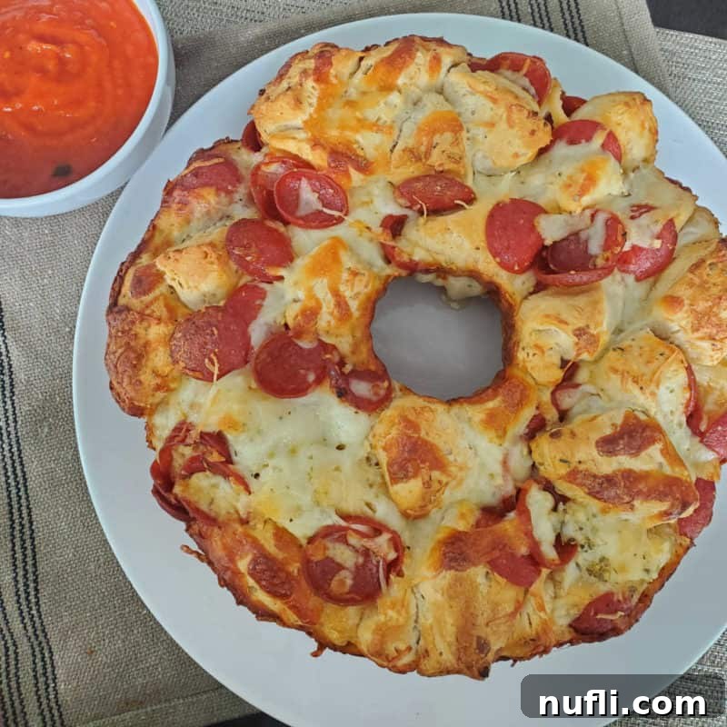 Pepperoni Pizza Monkey Bread, a delicious pull-apart creation, presented on a white plate alongside a small bowl of savory marinara sauce.