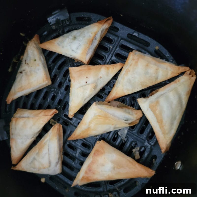 Golden air-fried spanakopita triangles, perfectly crispy and inviting, arranged neatly in an air fryer basket.
