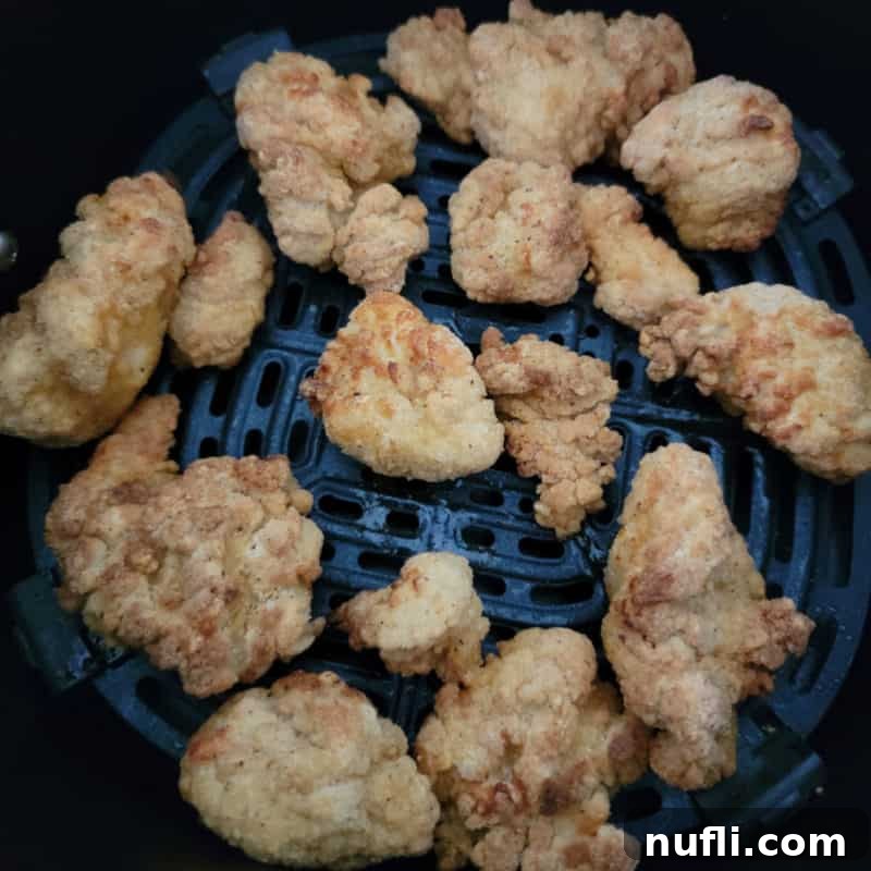 Crispy popcorn chicken, perfectly cooked and golden, spread out invitingly in an air fryer basket.