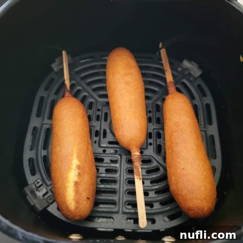 Three golden-brown air-fried corn dogs, perfectly cooked and crispy, arranged enticingly in an air fryer basket.