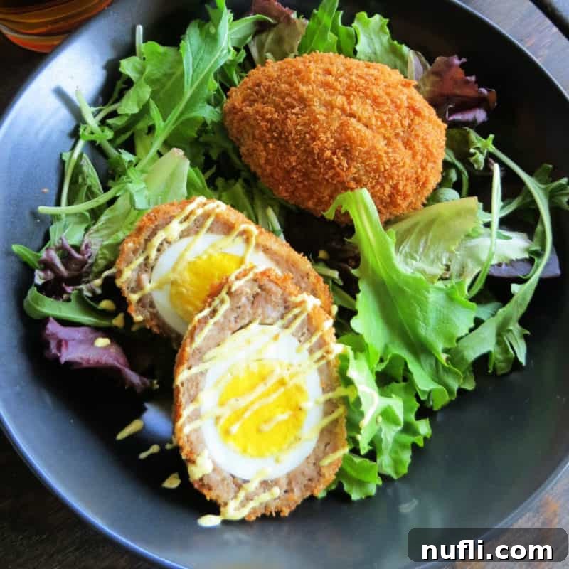 A pair of beautifully cooked Scotch Eggs, with their golden crust and savory interior, elegantly presented on a bed of fresh lettuce.