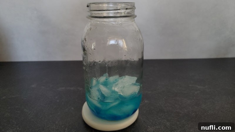 A blue liquid with ice cubes swirling inside a cocktail shaker, illustrating the chilling process for the Blue Balls Shot, preparing it for optimal enjoyment.