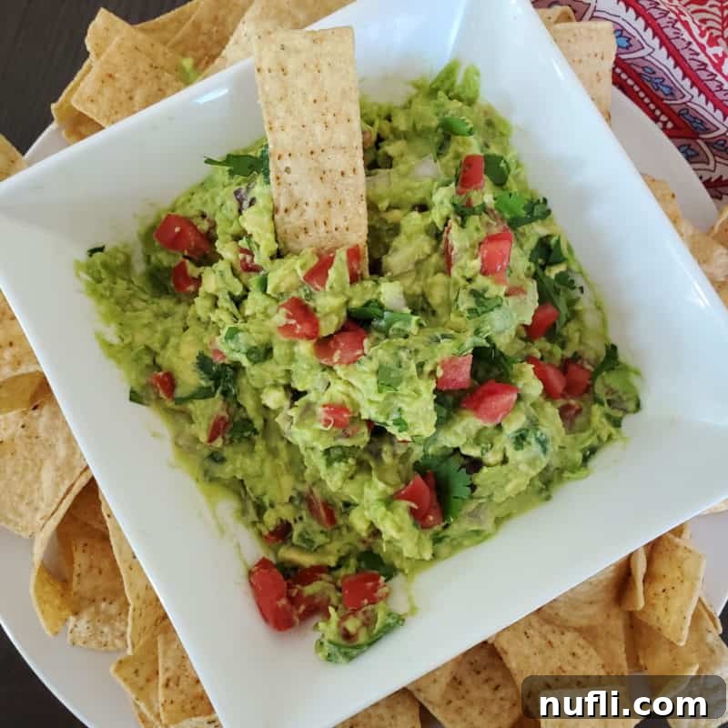 Guacamole with diced tomatoes in a white bowl with tortilla chips