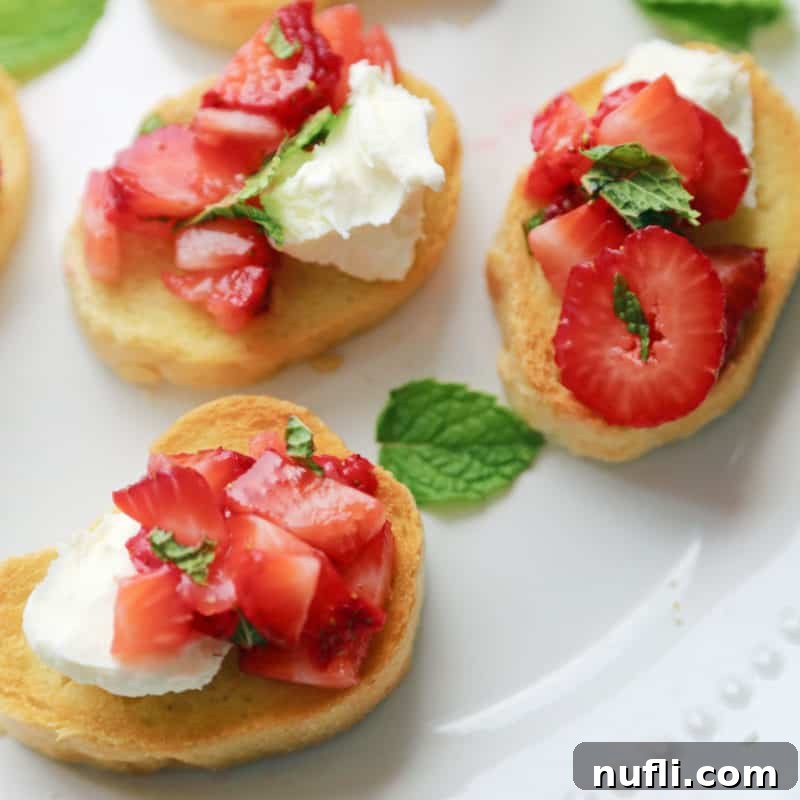 Slices of strawberry bruschetta on a white serving dish with mint leaves
