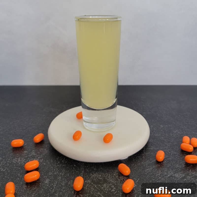 Vibrant Orange Tic Tac Shot in a stylish shot glass, surrounded by scattered orange Tic Tac candies on a clean white coaster, ready for a party.