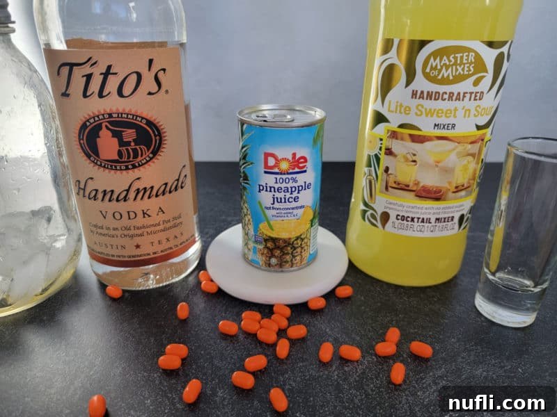 Arrangement of Tito's Vodka, vibrant Pineapple Juice, and Sweet 'n Sour Mix bottles alongside a clear shot glass and scattered orange Tic Tac candies, showcasing the simple ingredients for the Orange Tic Tac Shot.