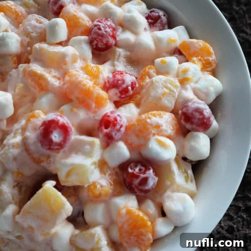Over 30 Essential Sides for Burger Enthusiasts 27 A colorful fruit salad featuring mandarins, pineapples, mini marshmallows, and cherries in a white bowl, offering a refreshing and sweet side.
