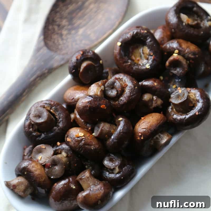 Over 30 Essential Sides for Burger Enthusiasts 28 Savory CrockPot Mushrooms served in a white dish with a wooden spoon, perfect as a side or burger topping.