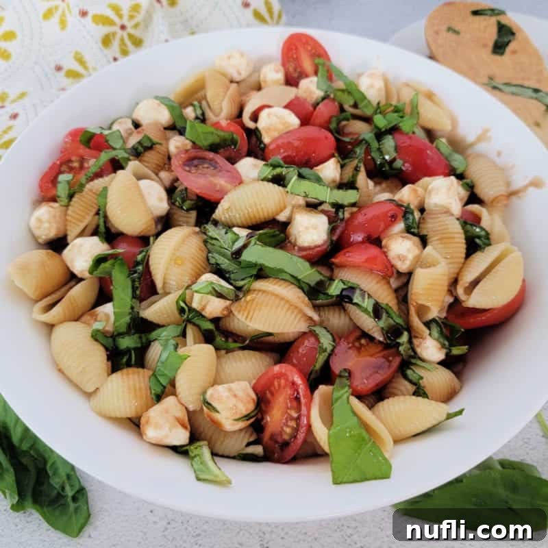 Over 30 Essential Sides for Burger Enthusiasts 5 A vibrant Caprese Pasta Salad in a white bowl, featuring cherry tomatoes, fresh mozzarella, and basil leaves, with a wooden spoon nearby.