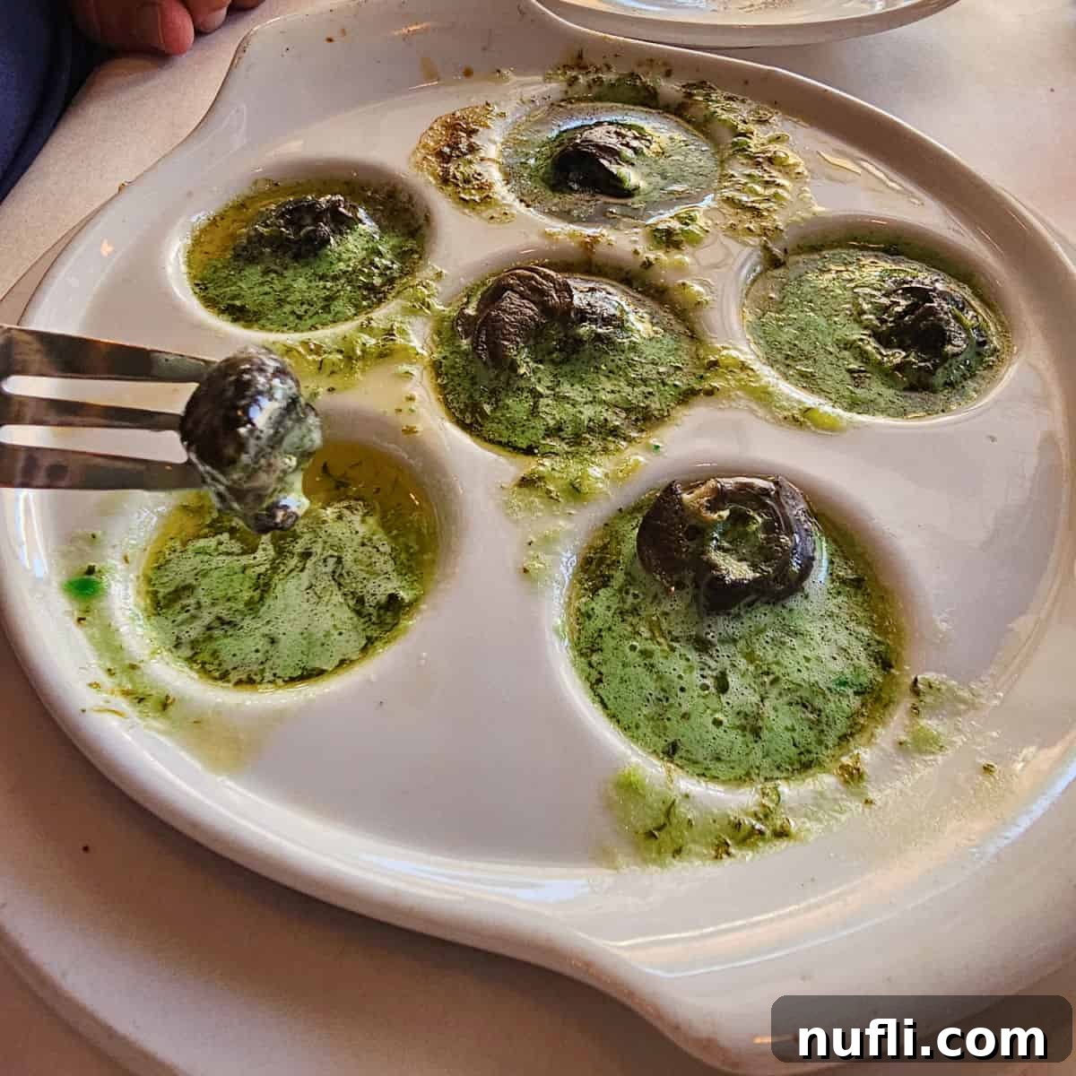 Exquisite escargot in a vibrant green butter sauce, served in a white dish with a fork.