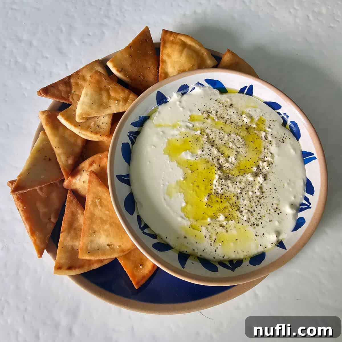 Whipped feta dip in a white and blue bowl on a blue plate with pita chips