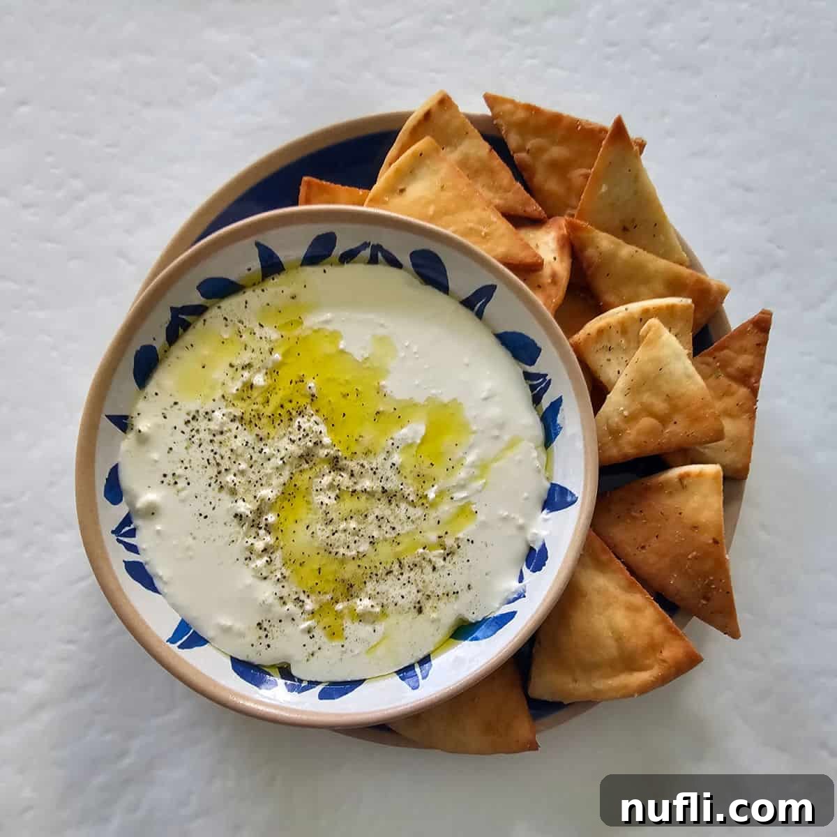 creamy whipped feta dip in a white and blue bowl sitting on a blue plate with pita chips