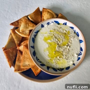 Whipped feta dip in a white and blue bowl on a blue plate with pita chips