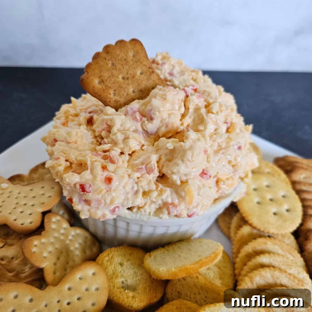 Pimento cheese in a white bowl on a plate with crackers