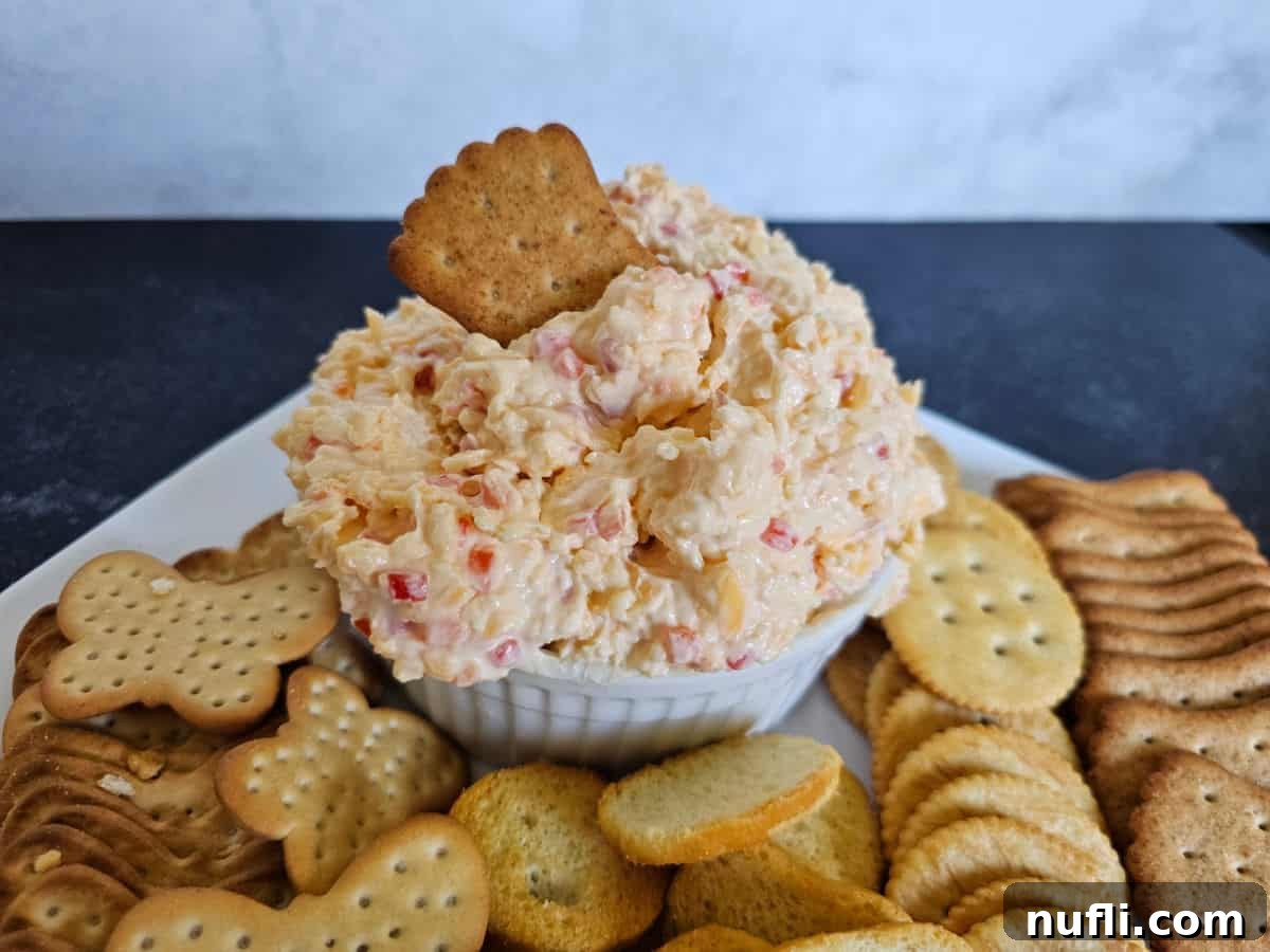 wheat cracker in a bowl of pimento cheese on a white plate filled with a variety of crackers