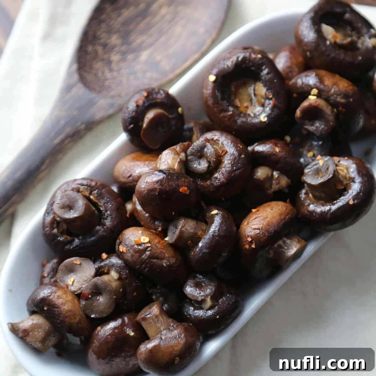 Flavorful Crockpot garlic mushrooms, served on a white serving dish with a wooden spoon, perfect as an appetizer or side.