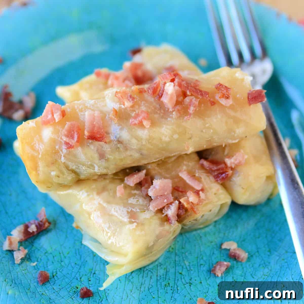 Savory Crockpot Cabbage Rolls, beautifully garnished with crispy bacon, served on a blue plate with a silver fork.
