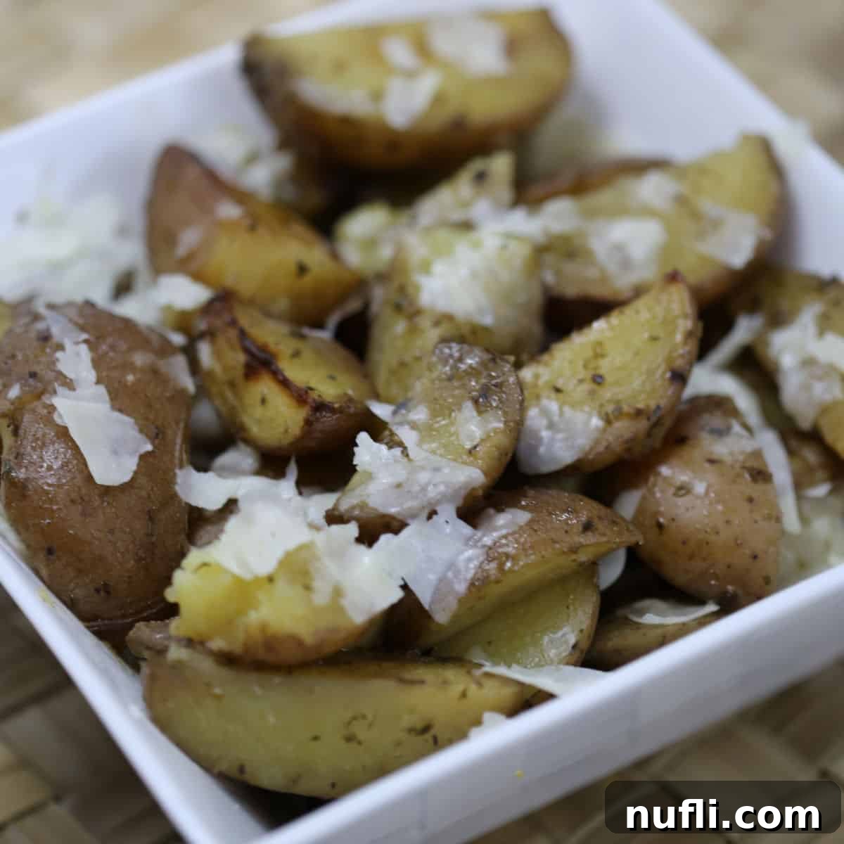 Golden brown parmesan potatoes cooked in a Crockpot, served in a white bowl and garnished with fresh herbs.