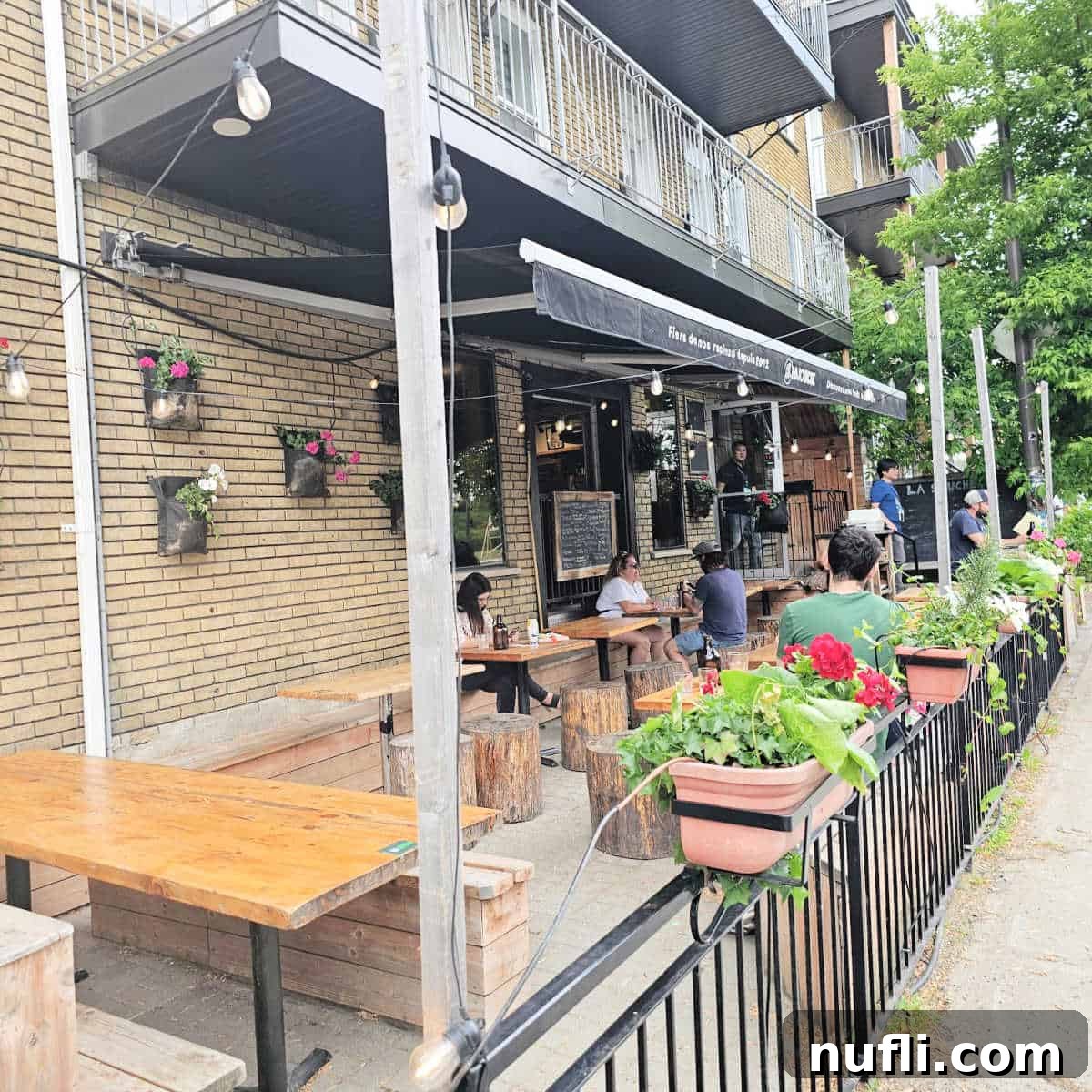 The inviting exterior of La Souche - Limoilou, featuring outdoor tables and chairs amidst lush plants along the railing