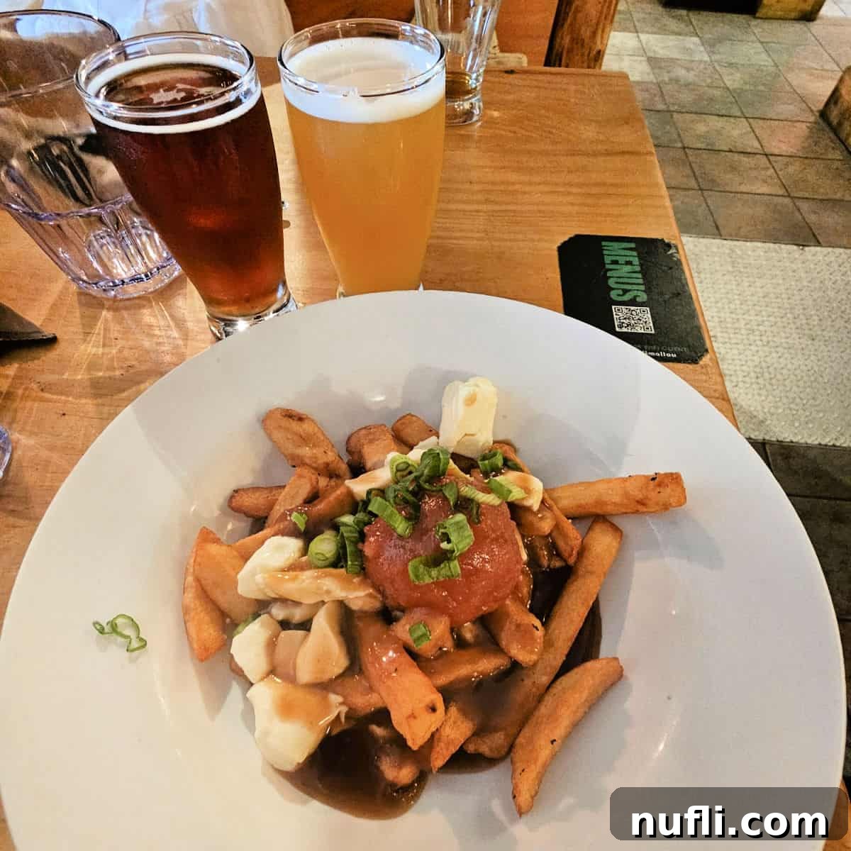 A generous serving of poutine, creatively topped with a fried 'lumberjack ball', accompanied by two glasses of craft beer