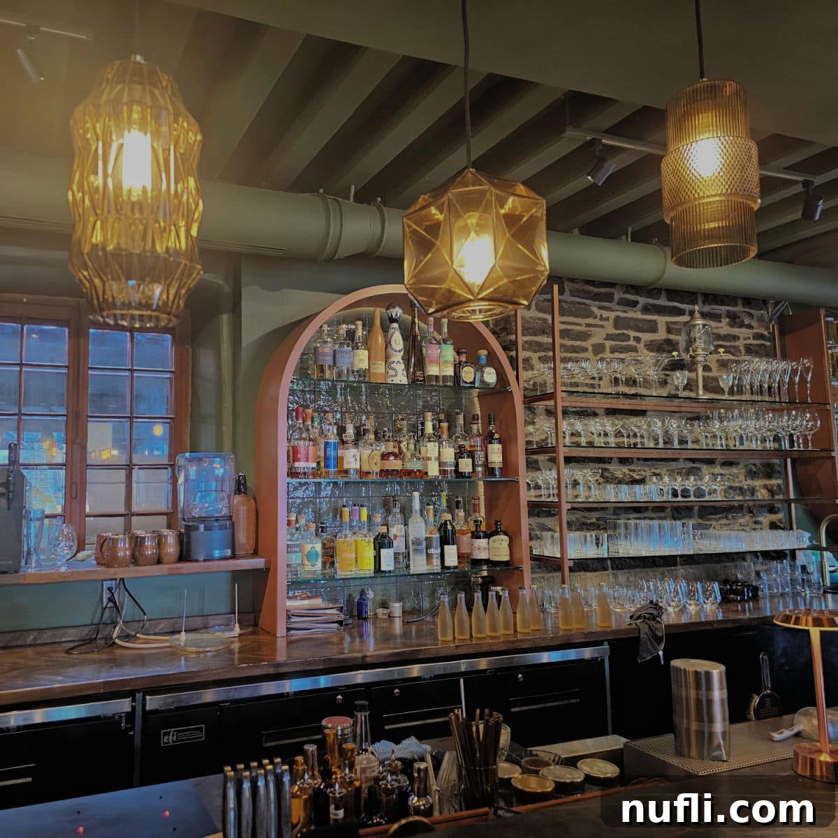 An elegantly stocked cocktail bar, featuring shelves laden with various liquors, glistening glassware, and an array of bottles, inviting patrons to enjoy a refined drink