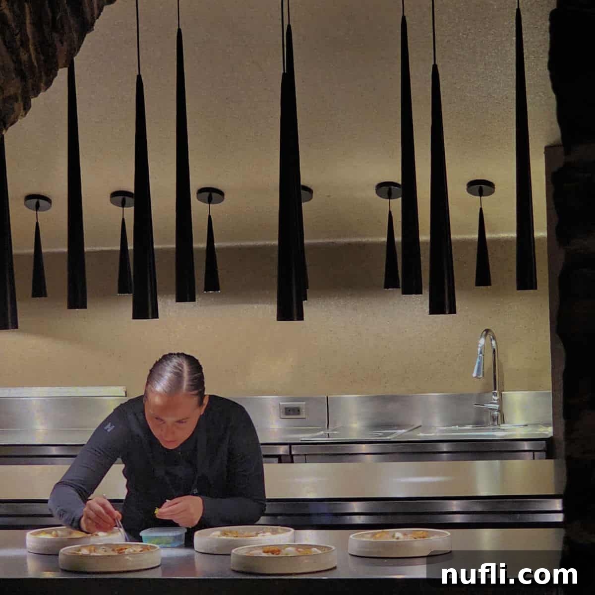 A chef meticulously plating a dish with tweezers in the refined setting of Restaurant Tanière³, showcasing precision and culinary artistry