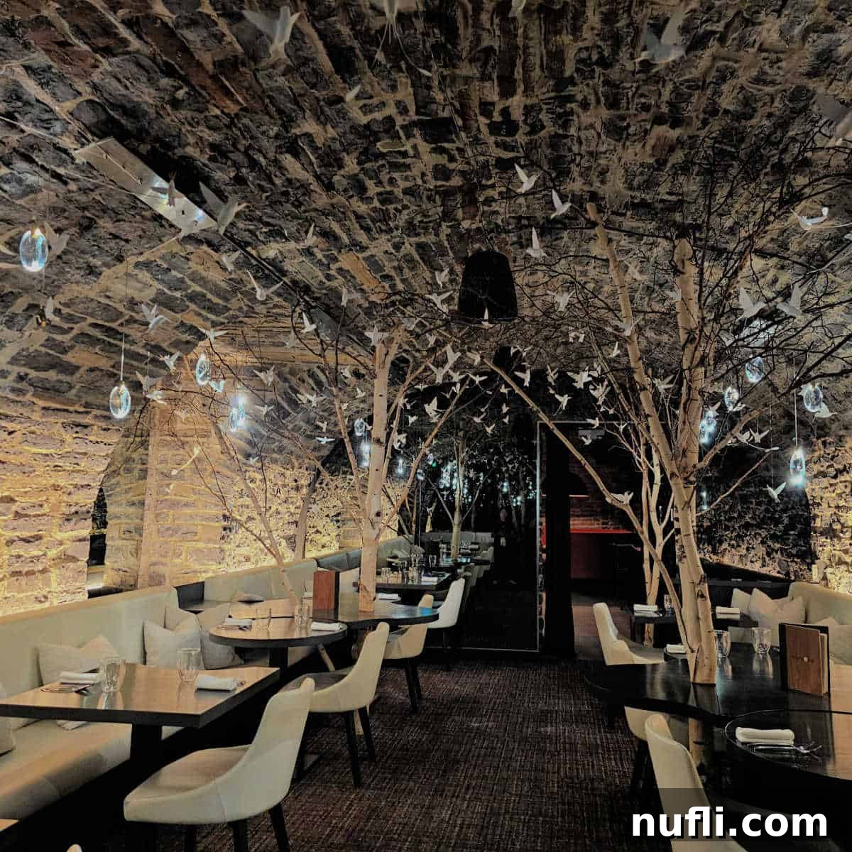 The unique cave-like dining room at Restaurant Tanière³, adorned with delicate paper birds and globes suspended from the ceiling, and furnished with elegant white tables and benches