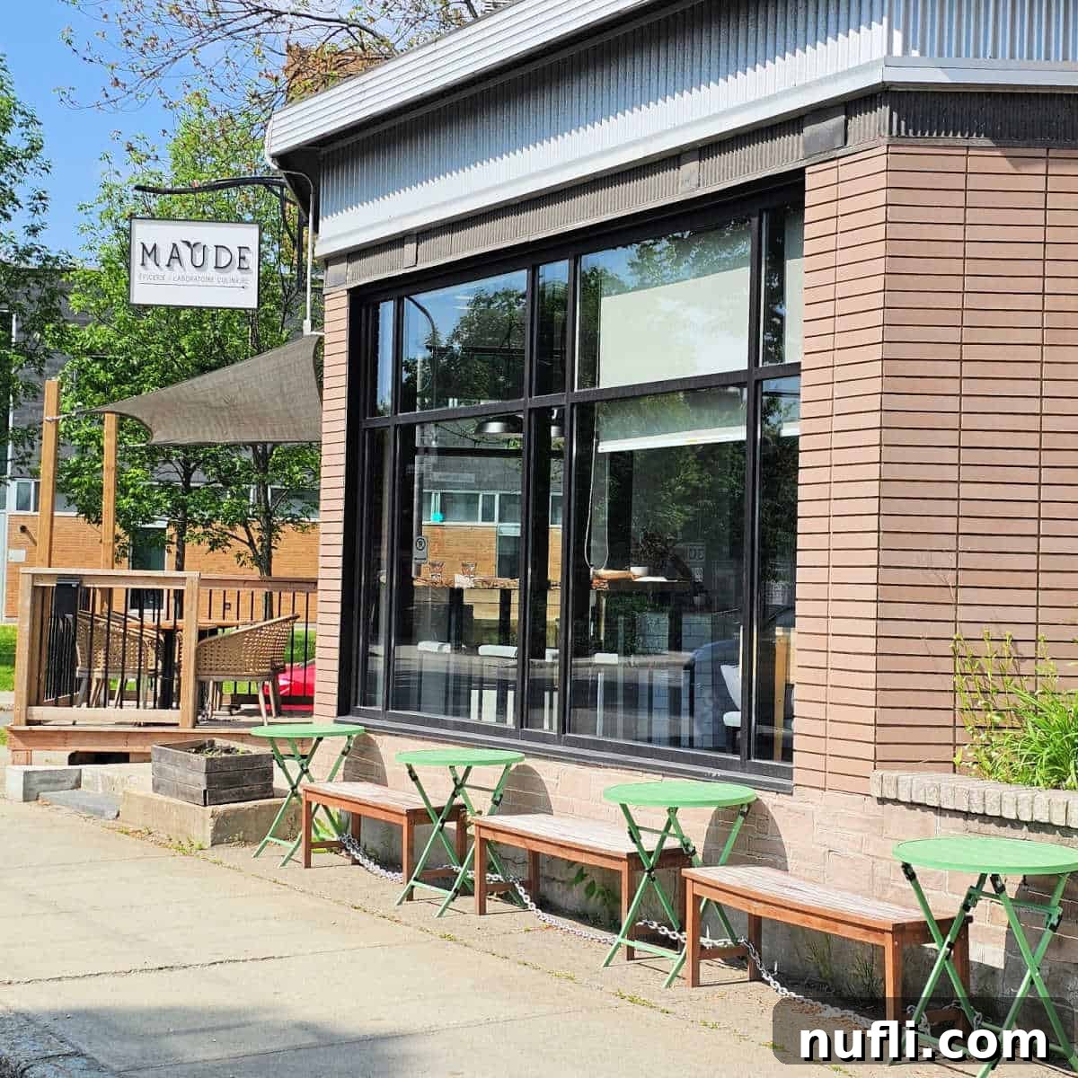 The charming exterior of Maude Épicerie/Laboratoire Culinaire, featuring its distinctive sign, inviting outdoor tables, and benches
