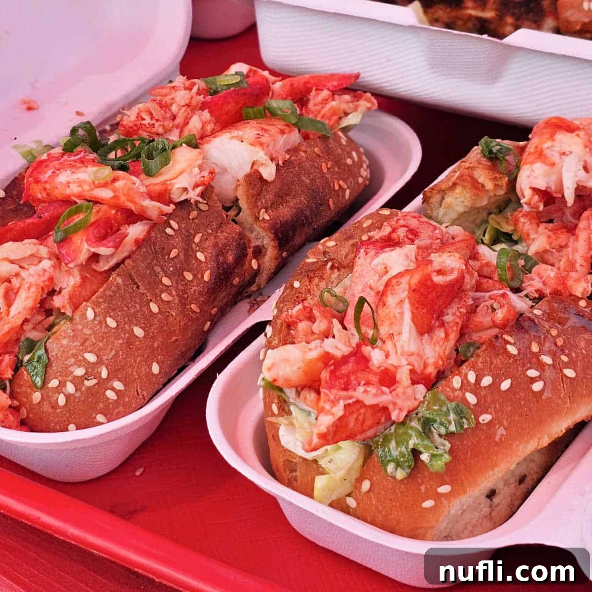 Two generously filled lobster rolls served in containers on a bright red tray, showcasing their fresh appeal