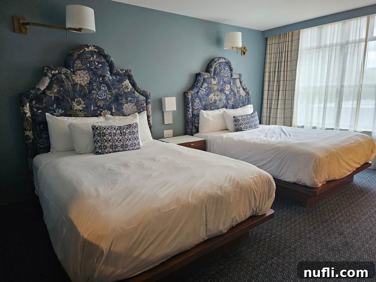 two queen beds with white linens, blue padded headboard